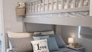 Ein Stockbett mit weißem Gestell, einer grauen gesteppten Bettdecke und einer blauen Tagesdecke.