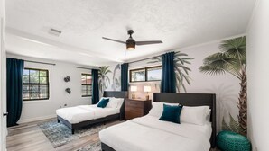 Un dormitorio con dos camas, un ventilador de techo y un ventanal con cortinas.
