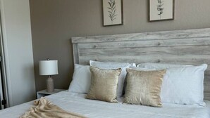 Quarto de hotel com uma cama, mesa de cabeceira, abajur e dois desenhos de folhas emoldurados na parede.