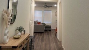 Corredor que dá para uma sala de estar com ventilador de teto, sofá e mesa de jantar com cadeiras.