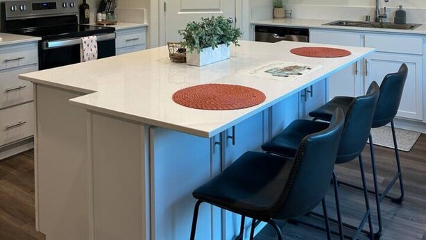 Uma cozinha moderna com armários brancos, uma ilha central com banquetas, micro-ondas e pia.