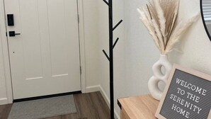 Um corredor com um porta-roupas, uma placa de boas-vindas e uma porta.