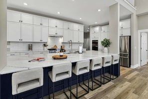 A modern kitchen with white cabinets, a marble island, and bar stools.