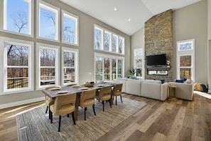 A spacious living area with a stone fireplace, large windows, and a dining table set for six.