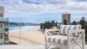 A balcony with a view of a beach and ocean, a striped chair, and a high-rise building in the background. - Saltview, Queenscliff (Queenscliff)