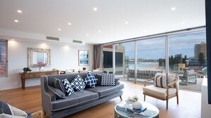 A modern living room with a grey sofa, patterned cushions, a coffee table, and a large glass door leading to a balcony with a city view. - Saltview, Queenscliff (Queenscliff)