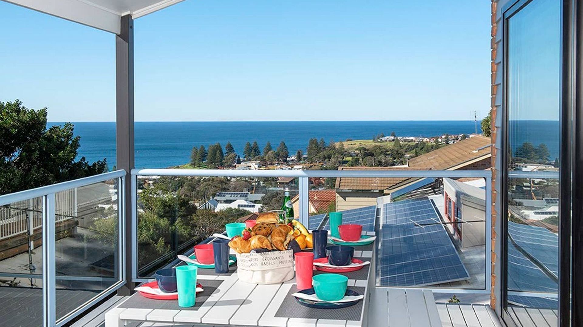 A balcony with a table set for breakfast, overlooking a coastal view.