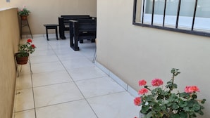Un balcon carrelé, agrémenté de plantes en pot et d’un banc noir.
