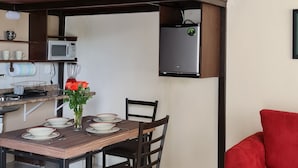 Un espace de vie compact comprenant un coin repas, une kitchenette et un canapé rouge.