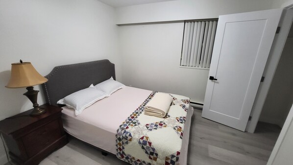 A bedroom with a bed, a nightstand, a lamp, a door, and a window with blinds. - House convinietly centered and easy access to all local attractions. (North Vancouver)