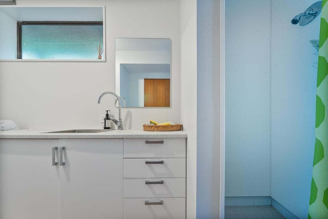 A modern bathroom with a white sink, mirror, and cabinets.