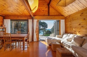Ein Holzinnenraum mit Essbereich, einer Couch und Blick durch ein großes Fenster.