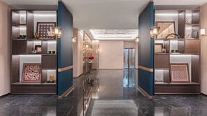 Un'accogliente hall d'hotel moderna, con pavimento in marmo lucido, scaffalature integrate e oggetti decorativi, illuminata da un lampadario centrale.