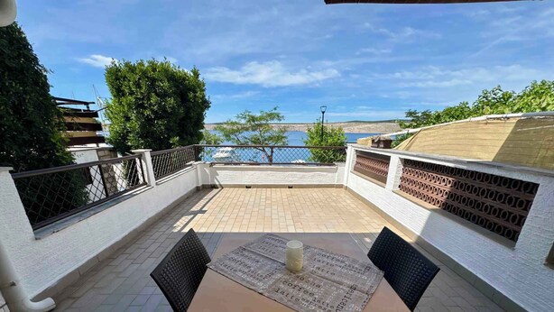 Un patio con mesa y sillas, vista al mar y un edificio blanco con pared de ladrillo.