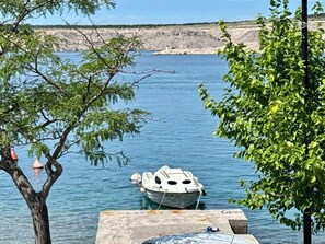 A boat docked at a pier with clear water and a rocky shoreline in the background. - Studio with a balcony directly by the sea (Jadranovo)