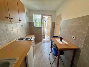 A compact kitchen with a stove, cabinets, and a dining area with chairs. - Studio with a balcony directly by the sea (Jadranovo)