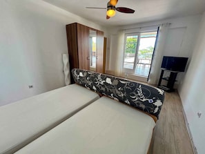 A room with a bed, a wardrobe, a ceiling fan, a TV stand, and a window with a view. - Studio with a balcony directly by the sea (Jadranovo)