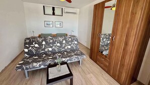 Una habitación con sofá, una mesita con un florero, ventilador de techo, armario y cuadros en la pared.