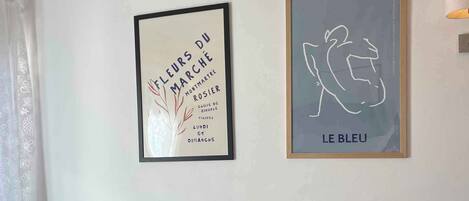 Un salon moderne avec un canapé en cuir noir, une table d’appoint en bois et deux œuvres d’art encadrées accrochées au mur.