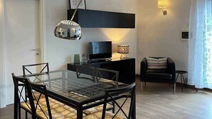 Ein modernes Wohnzimmer mit einem Glastisch, schwarzen Stühlen, einem schwarzen Sofa, einem Fernseher und einer Lampe.
