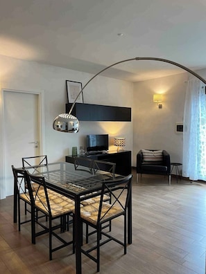 Ein modernes Wohnzimmer mit einem Glastisch, schwarzen Stühlen, einem schwarzen Sofa, einem Fernseher und einer Lampe.