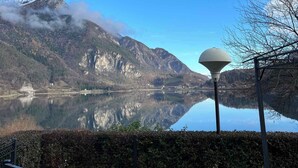 Ein ruhiger See mit Bergen im Hintergrund, einem klaren Himmel und einem Laternenpfahl im Vordergrund.