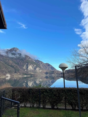 Ein ruhiger See mit Bergen im Hintergrund, einem klaren Himmel und einem Laternenpfahl im Vordergrund.