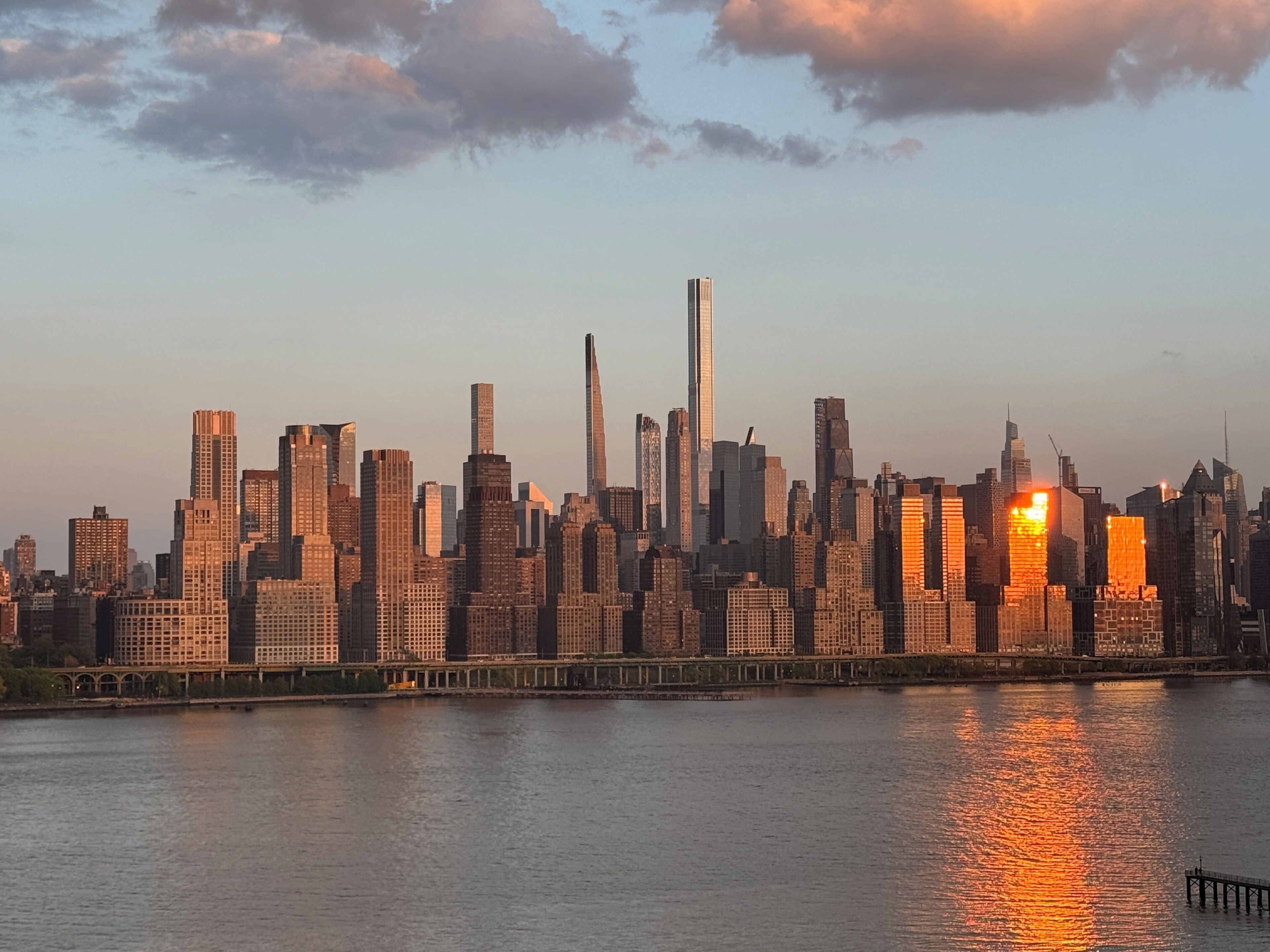A city skyline with high-rise buildings, a body of water in the foreground, and a bridge.