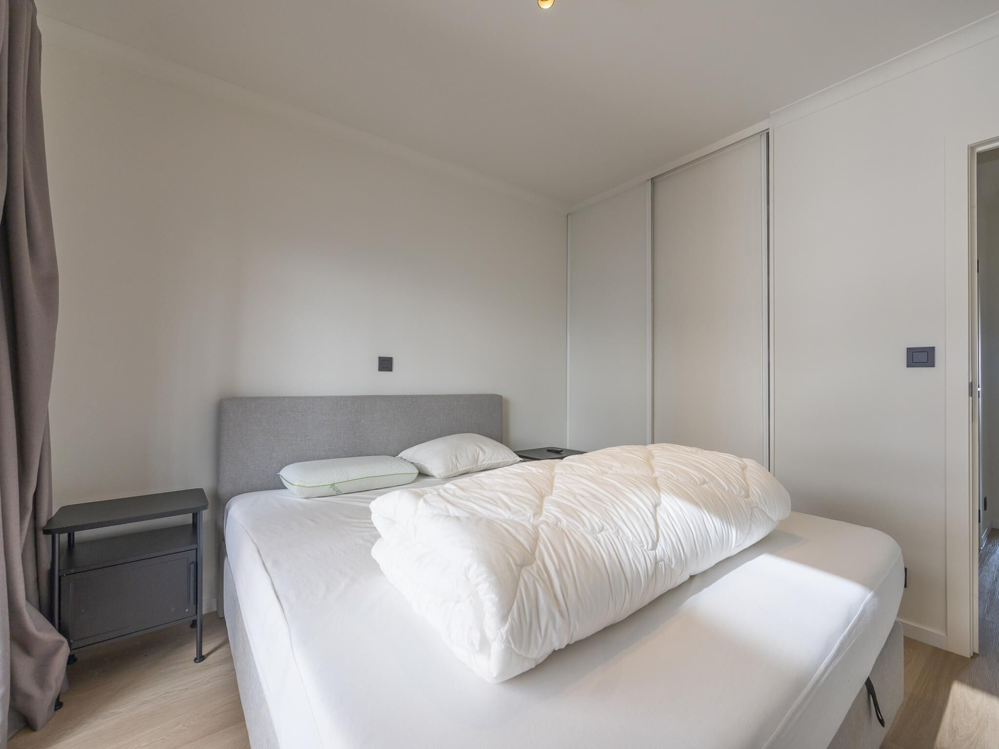 A modern bedroom with a bed, bedside tables, and a wardrobe.