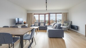 Ein modernes Wohnzimmer mit Essbereich, großen Fenstern und Blick auf die Stadt.
