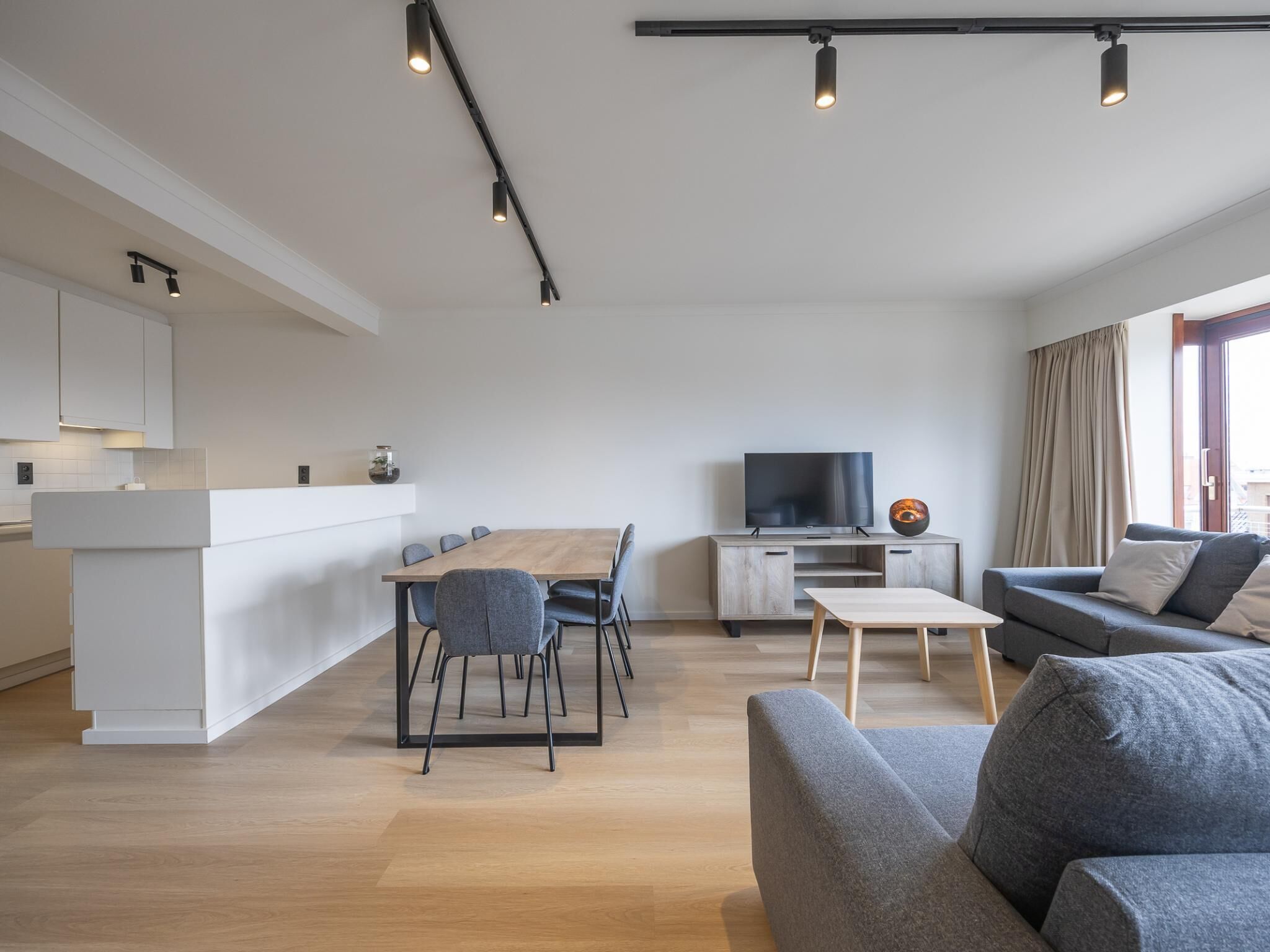 Ein modernes Wohnzimmer mit Sofa, Fernseher, Esstisch und Küchenzeile.