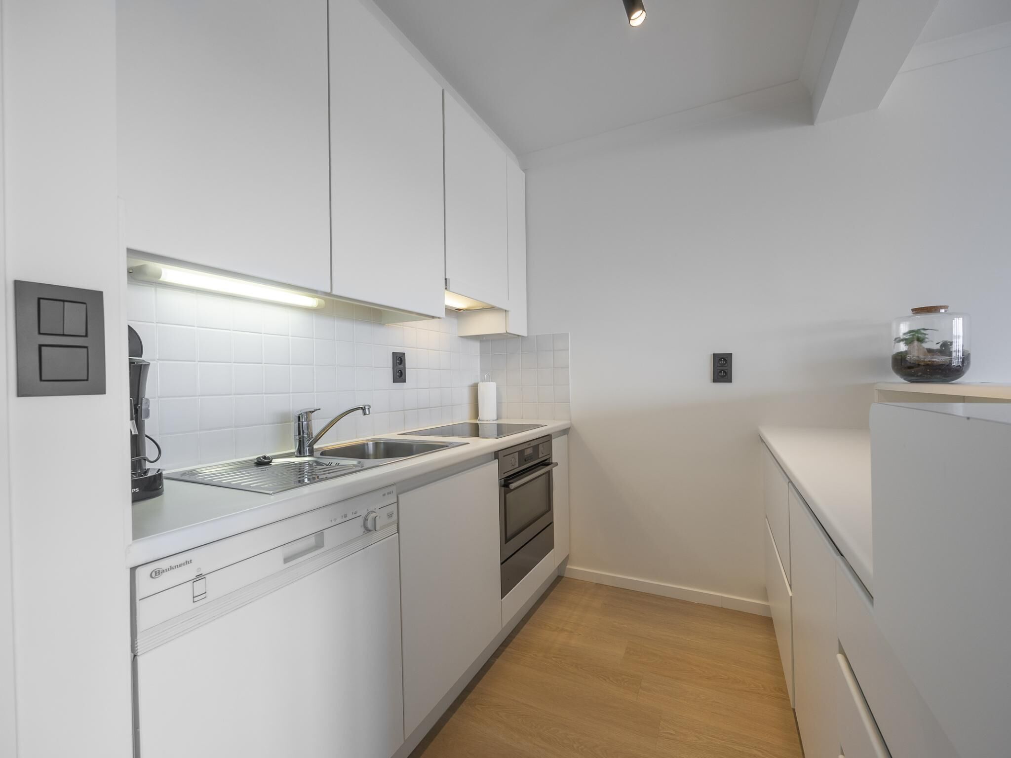 A modern kitchen with white cabinets, a stainless steel sink, and a built-in oven.