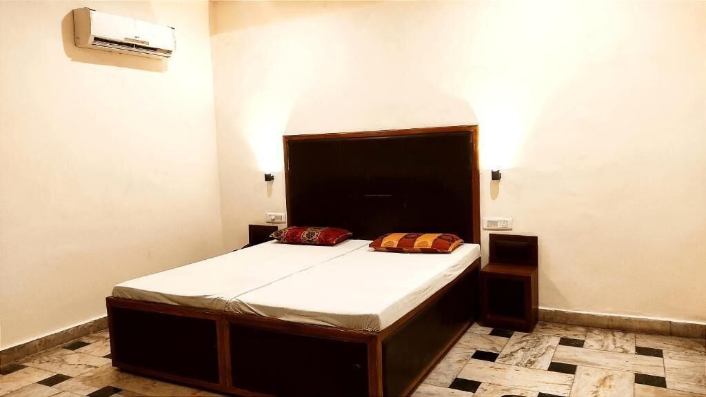 Una cama individual con estructura de madera, dos mesitas de noche, un aire acondicionado instalado en la pared y un suelo con diseño.