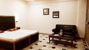 A room with a bed, a black leather chair, a small wooden table, and two framed pictures on the wall. - HOTEL INTERNATIONAL (Jalandhar)
