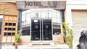 A hotel entrance with a glass facade, a sign reading 'HOTEL INTERNATIONAL,' and a reflection of a car in the window. - HOTEL INTERNATIONAL (Jalandhar)