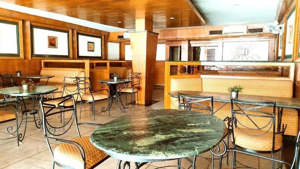 A restaurant with round tables and cushioned chairs, wooden walls, and framed pictures. - HOTEL INTERNATIONAL (Jalandhar)