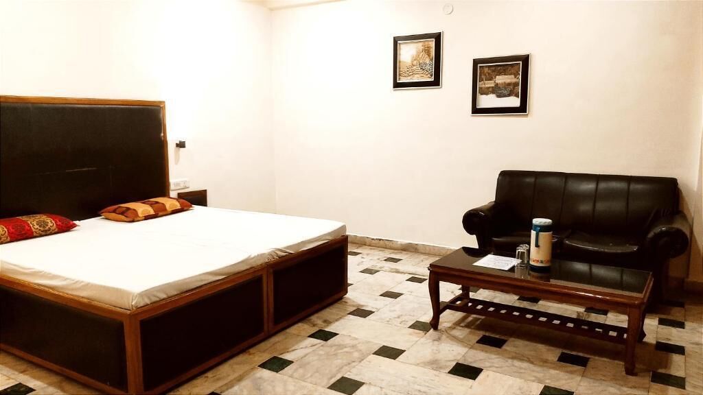 A bedroom with a bed, a black leather sofa, a coffee table, and two framed pictures on the wall.