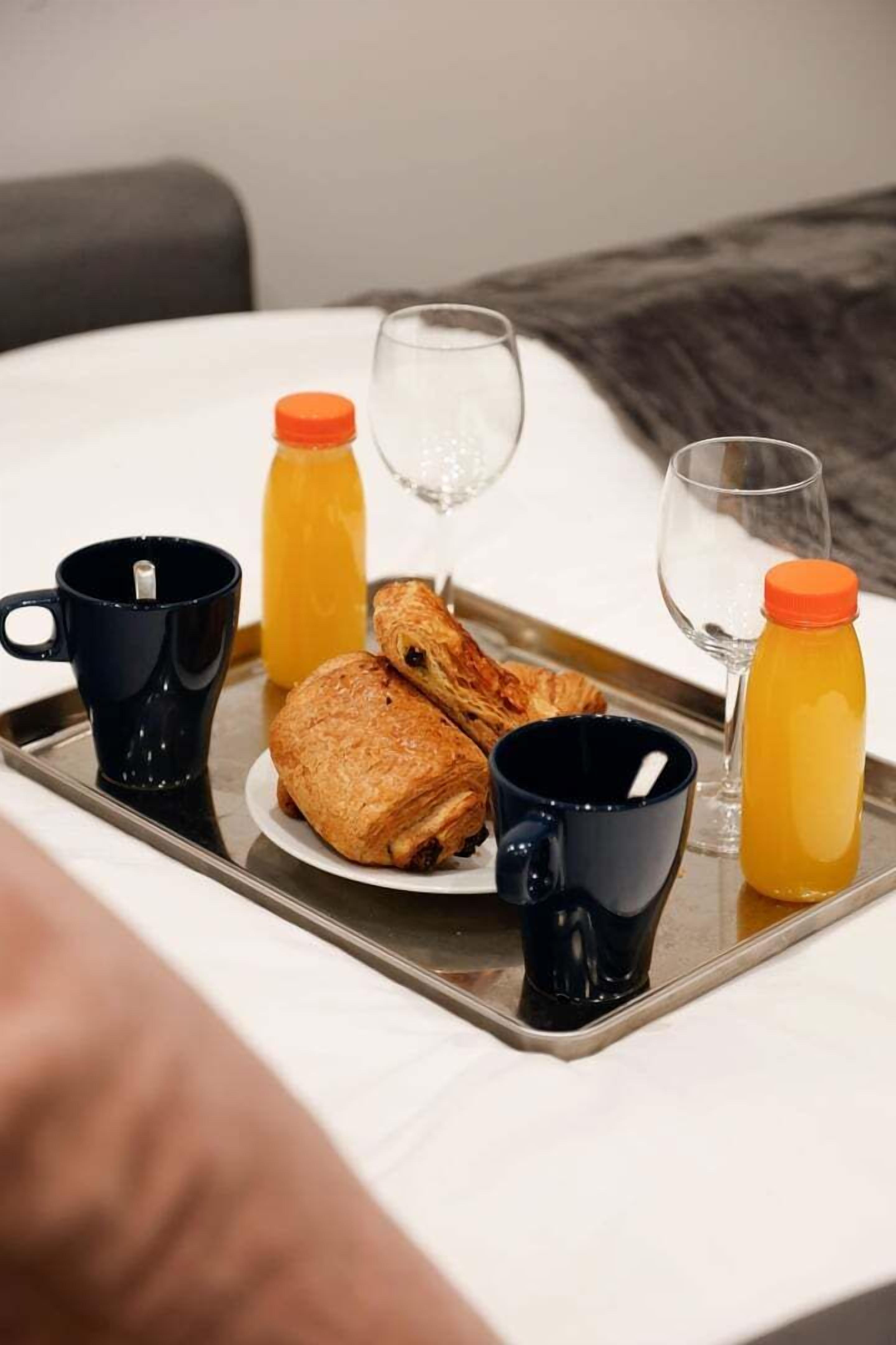 A breakfast tray with croissants, juice bottles, and coffee mugs on a bed.