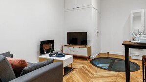 Un salon moderne comprenant un téléviseur à écran plat, une table à manger avec des chaises, un canapé et une petite table ronde avec un plateau en verre.