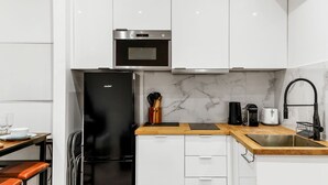 Une cuisine moderne avec des armoires blanches, un réfrigérateur noir, un four à micro-ondes et un pare-feu en marbre.