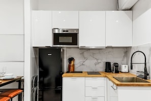 A modern kitchen with white cabinets, a black refrigerator, a microwave, and a marble backsplash. - TheBlueStay 259 - Stunning Apartment in Paris 4 (Paris)