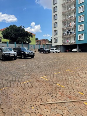 A parking area with multiple vehicles, a paved surface, and a multi-story building with balconies. - 2BR 1BA apartment near Kitintale Market Kampala with Wi-Fi, AC (Kampala)