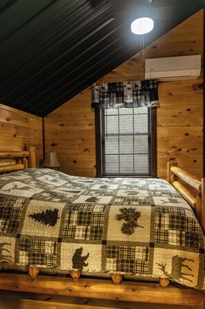 Quarto de cabana de madeira com cama, janela com persianas, ventilador de teto e unidade de ar condicionado.