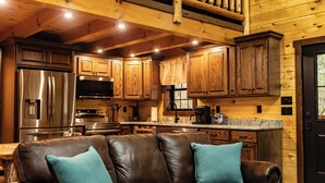 L’intérieur d’une cabane avec une terrasse en bois, une cuisine et un canapé en cuir agrémenté de coussins turquoise.