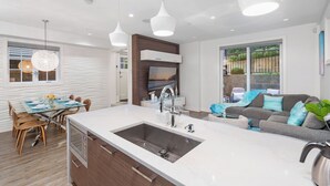A modern kitchen with a central island, a dining area with a glass table, and a living area with a sofa and TV. - Kitsilano Retreat: Private 3-Bed w/ Parking & BBQ (Vancouver)