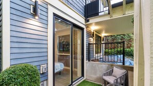 A modern building with a balcony, a glass door leading to a room with a bed, and a small outdoor seating area. - Kitsilano Retreat: Private 3-Bed w/ Parking & BBQ (Vancouver)
