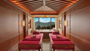 A spa room with wooden paneling, two massage tables, a large window with a mountain view, and wall-mounted lighting. - Welcomhotel By ITC Hotel Denzong Regency (Gangtok)