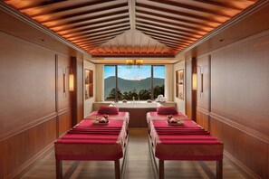 A spa room with wooden paneling, two massage tables, a large window with a mountain view, and wall-mounted lighting. - Welcomhotel By ITC Hotel Denzong Regency (Gangtok)
