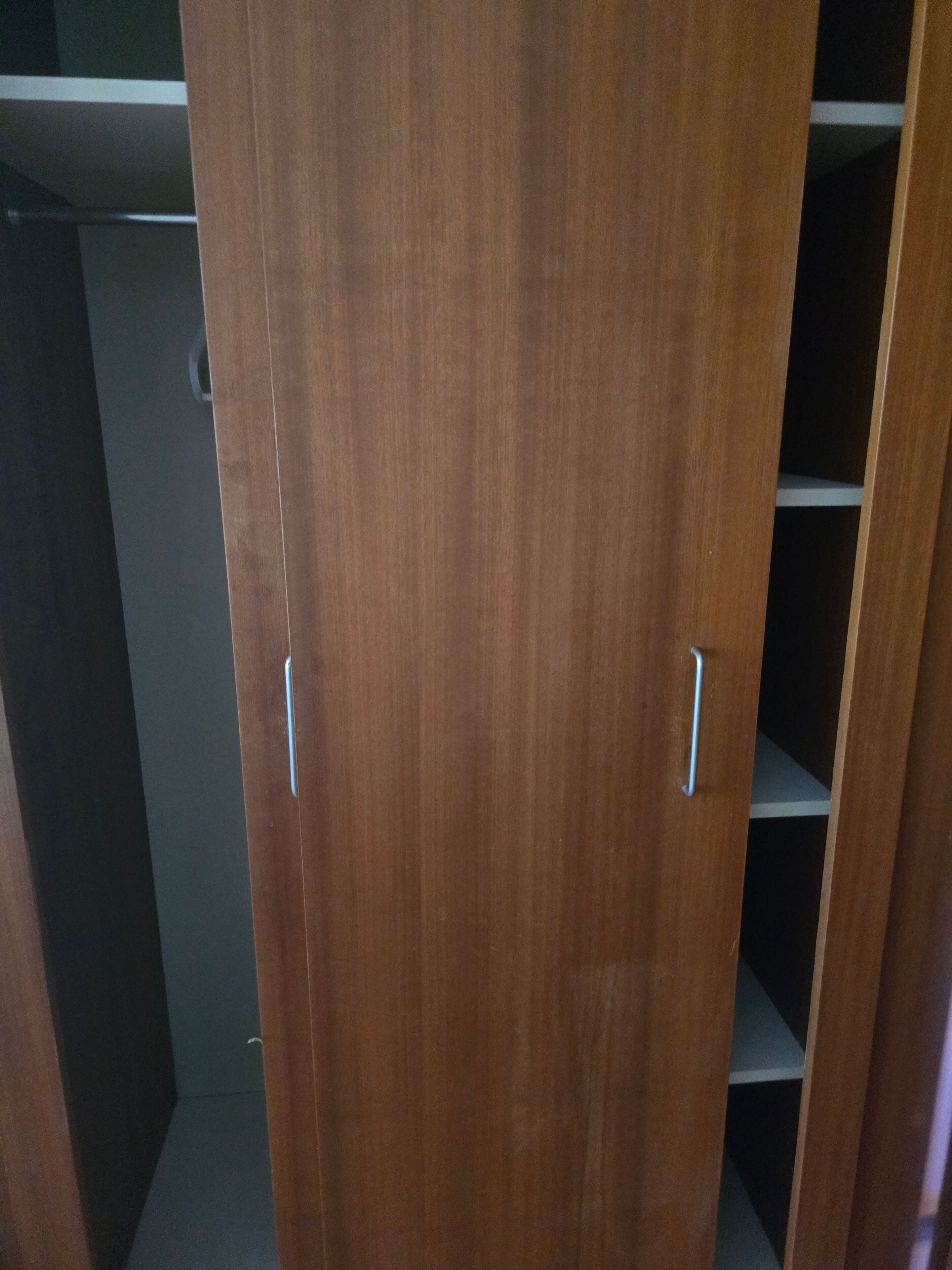 Ein Holzschrank mit zwei Griffen, dunklem Innenraum und einer sichtbaren Ablagefläche.