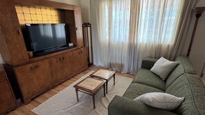 Een woonkamer met een houten tv-meubel, een groene bank, een salontafel en een vloerlamp.